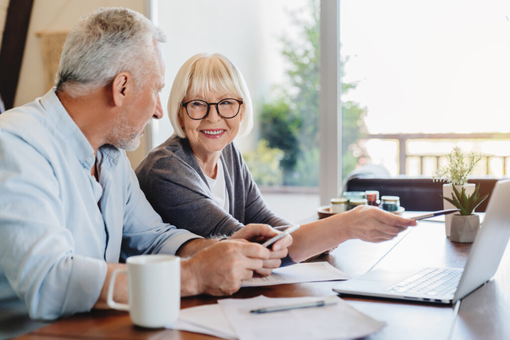 Senior couple happily doing annual tax return using laptop indoors