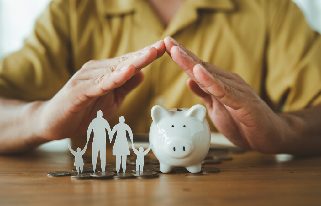 mortgage protection image showing woman's hands making a house shape over a piggy bank and paper doll family