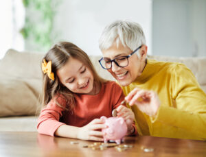 grandmother helping to teach her happy granddaughter how to save using a piggy bank on table