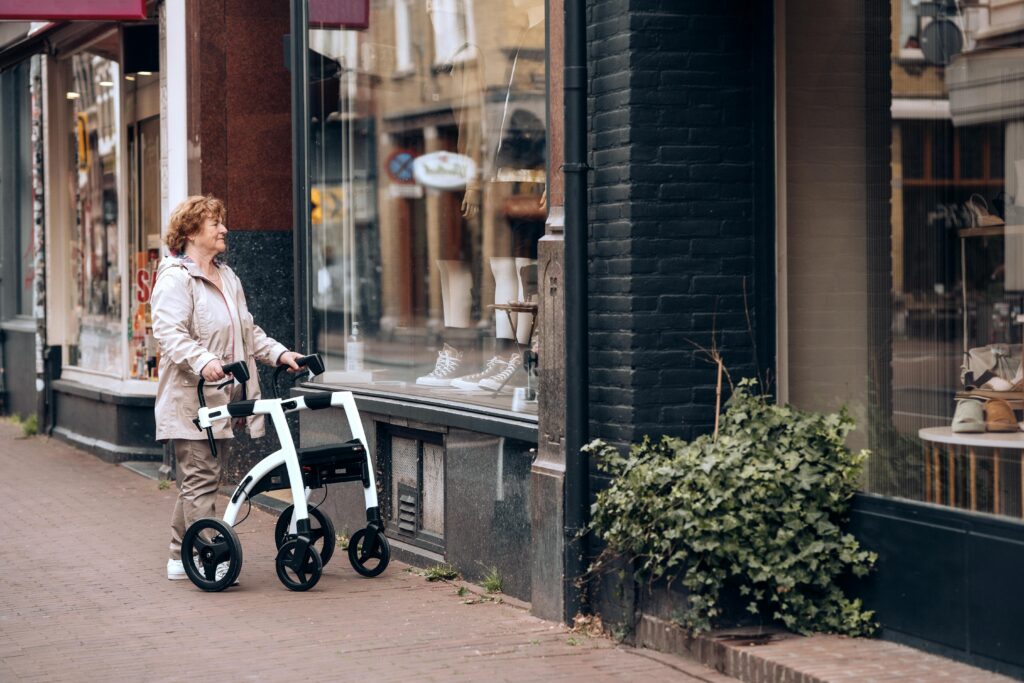 A woman with a walker window shops on a cobblestone street, looking at an apparel store with mannequins in the front displaying clothes.