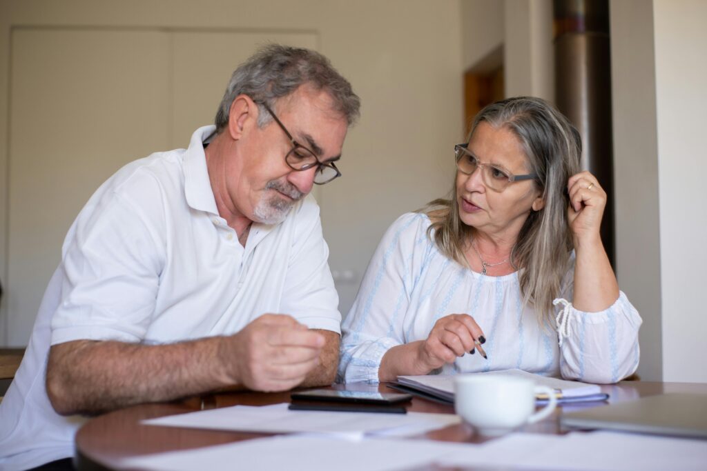 how much money do yu need for retirement? An older couple talks to each other while planning out their finances on a piece of paper and a smartphone.