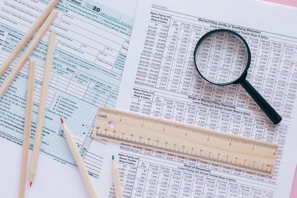 Six pencils, a wooden ruler, and a magnifying glass sit on top of several tax forms.