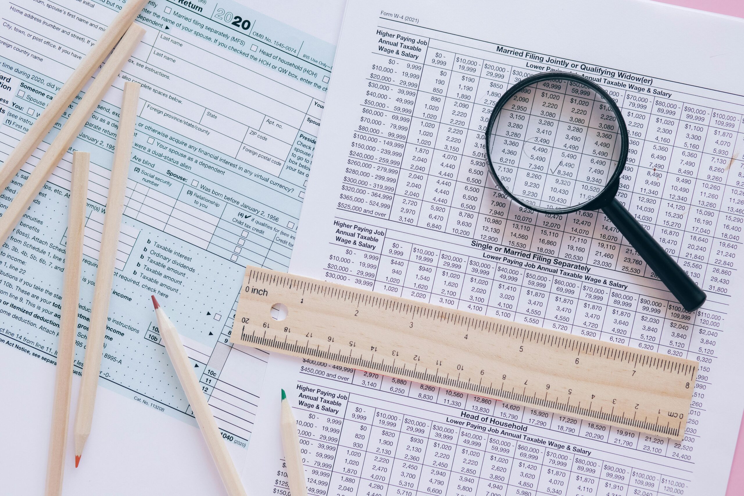pexels-leeloothefirst-8970296 | My Guide to Retirement Six pencils, a wooden ruler, and a magnifying glass sit on top of several tax forms.