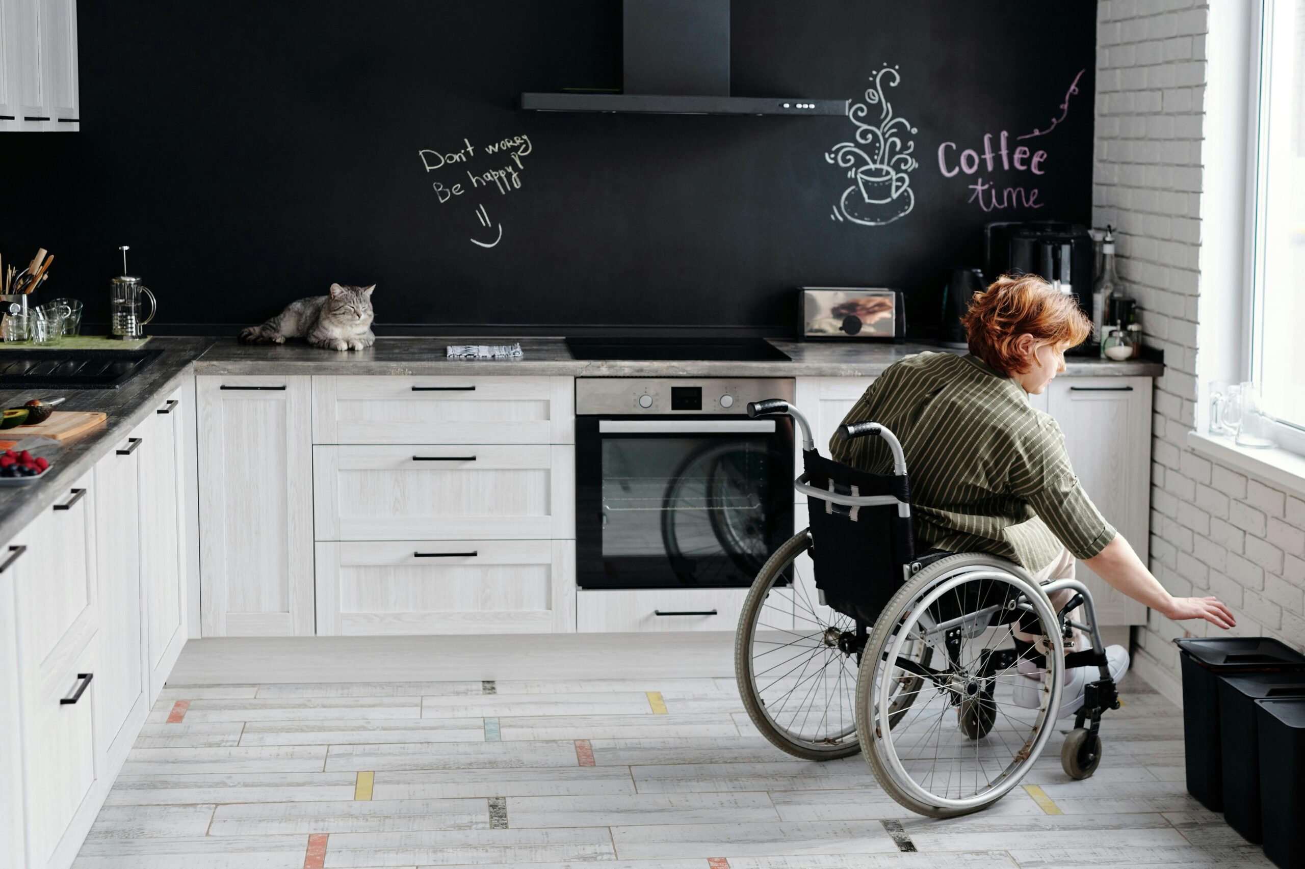 pexels-marcus-aurelius-4064416 | My Guide to Retirement A woman in a wheelchair is in her kitchen. The kitchen is modified so as to be handicap accessible.