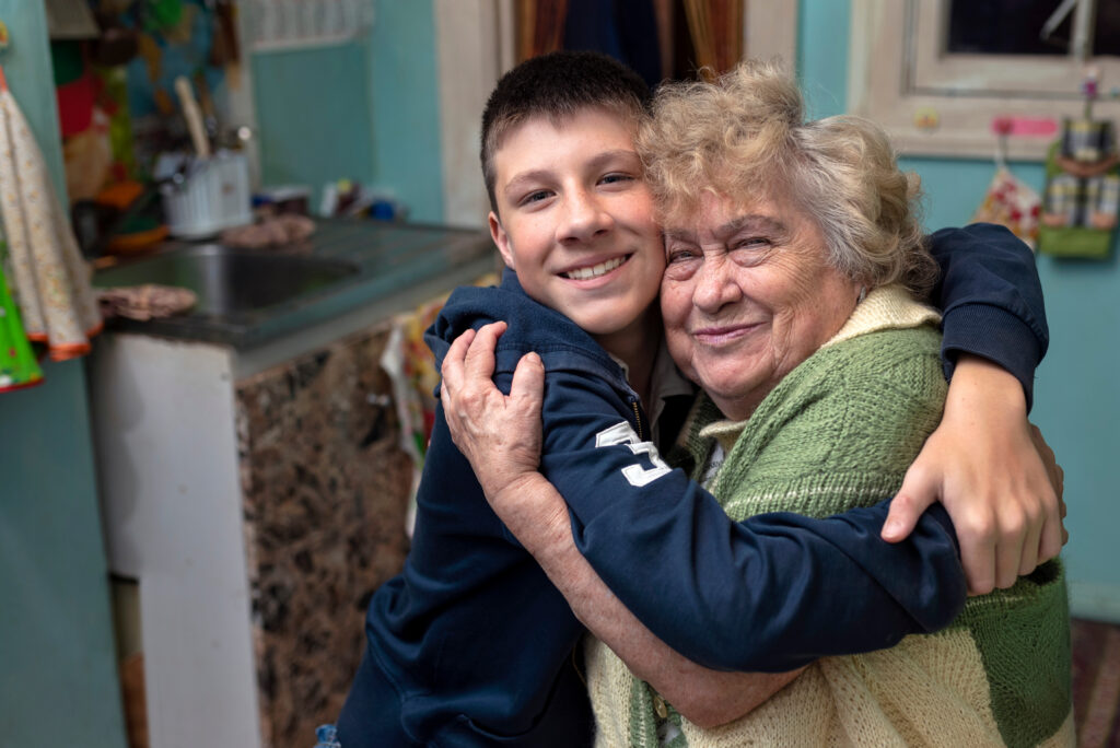 Senior on a fixed income hugging grandson happily looking at viewer
