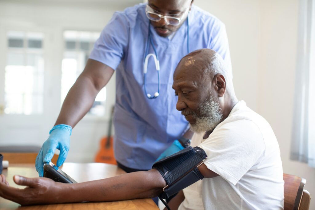 A healthcare provider wearing scrubs takes the blood pressure of an older patient.