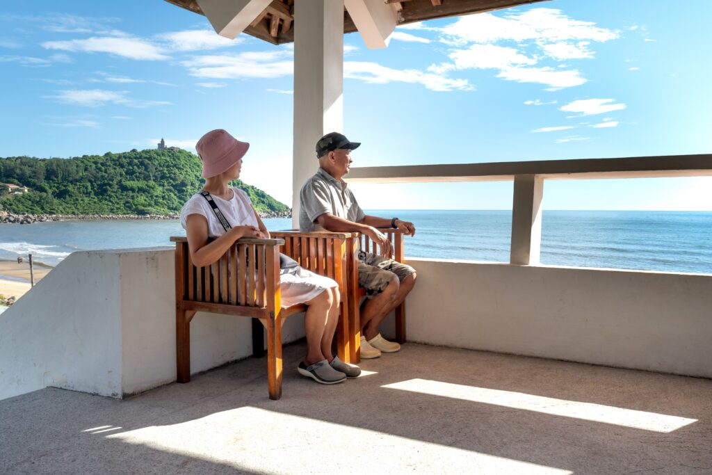 A couple enjoying a peaceful seaside view from a shaded terrace.
