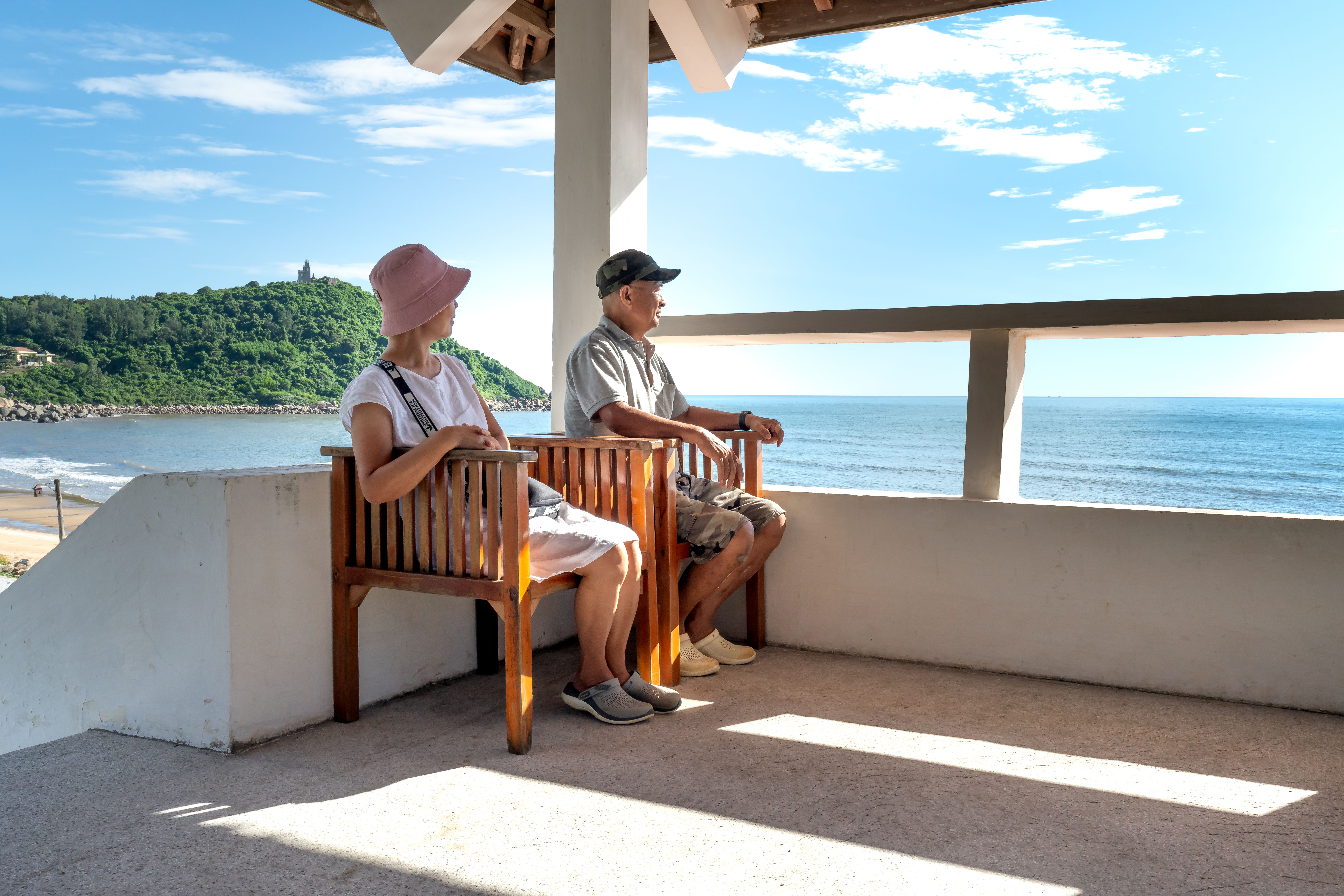 A couple enjoying a peaceful seaside view from a shaded terrace.